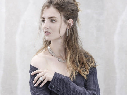Modelo usa colar triângulo prata feminino da Carmo Joalheiros com brincos e anéis em look casual